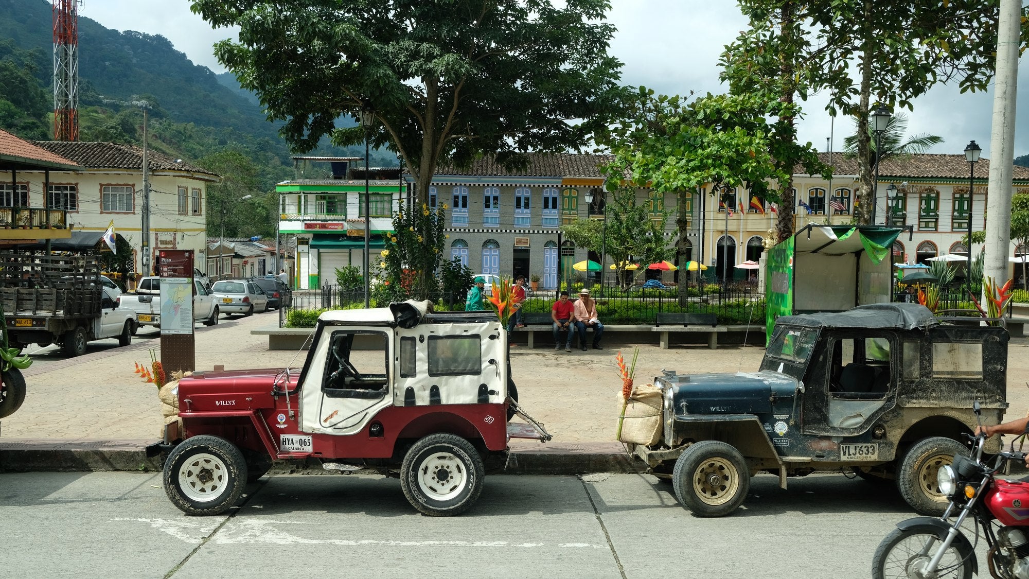 Two Willys jeeps parked on the square in Pijao, mountains behind